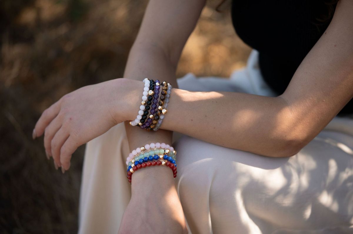 Arms resting on a knee, both wrists stacked with crystal and gold bracelets