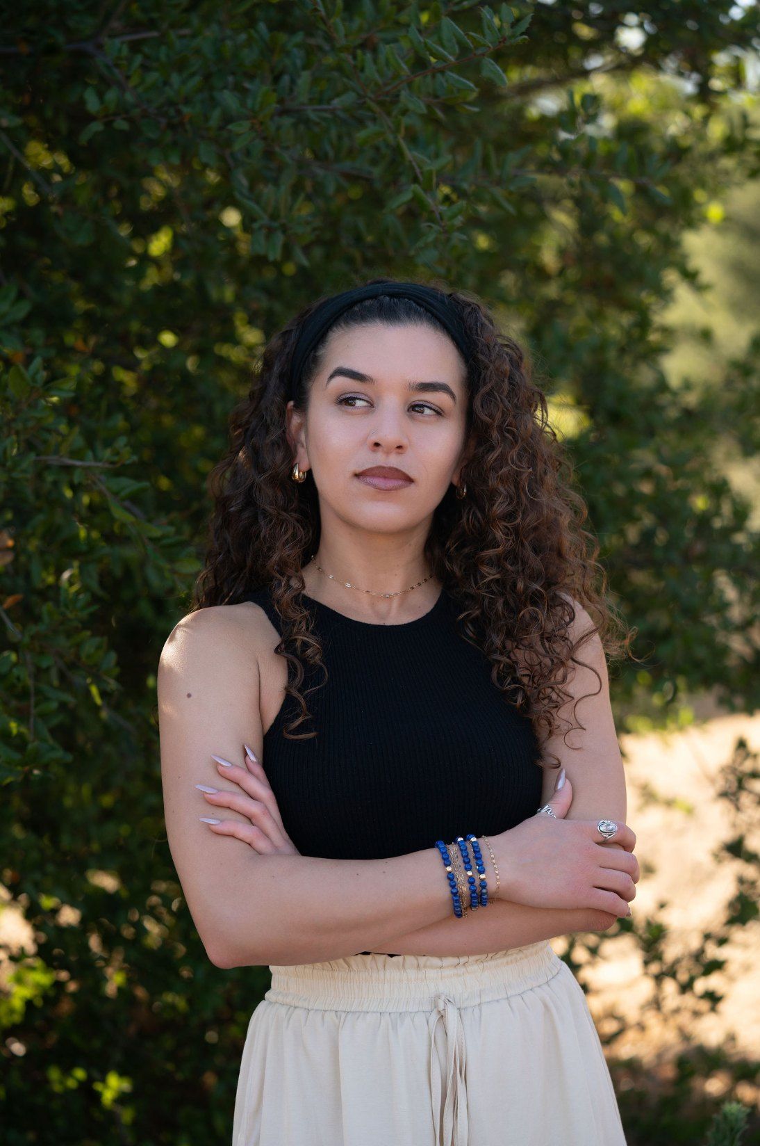 Char-Leen standing among the trees with her arms crossed, looking away